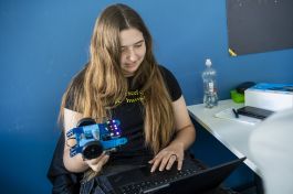 Schülerin programmiert am Laptop und hält Roboter in der Hand