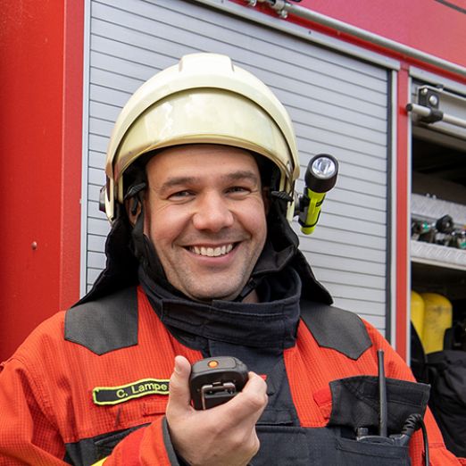 DVZ-Mitarbeiter Christian Lampe im Feuerwehranzug vor einem Feuerwehrauto stehend