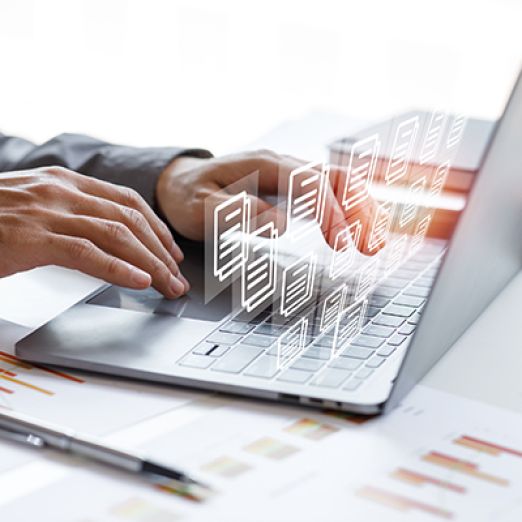 1)	Bild: Eine Person schreibt mit der einer Hand auf einem Laptop und nutzt mit der anderen das Touchpad. Über dem Laptop schweben mehrere Symbole von Dokumenten. 