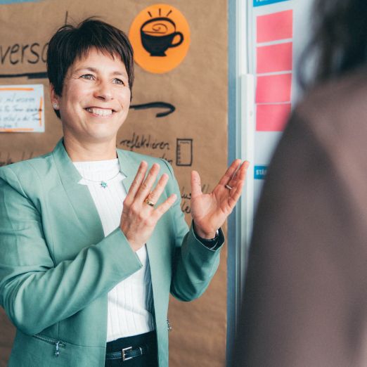 Change Managerin Romy Reitz erklärt etwas vor einer Metaplanwand.