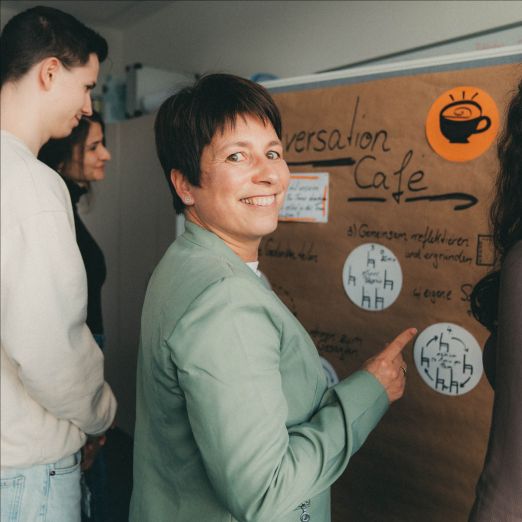 Change Managerin Romy Reitz zeigt auf eine Metaplanwand, während andere DVZ-Kolleginnen und -Kollegen auf die Metaplanwand schauen.