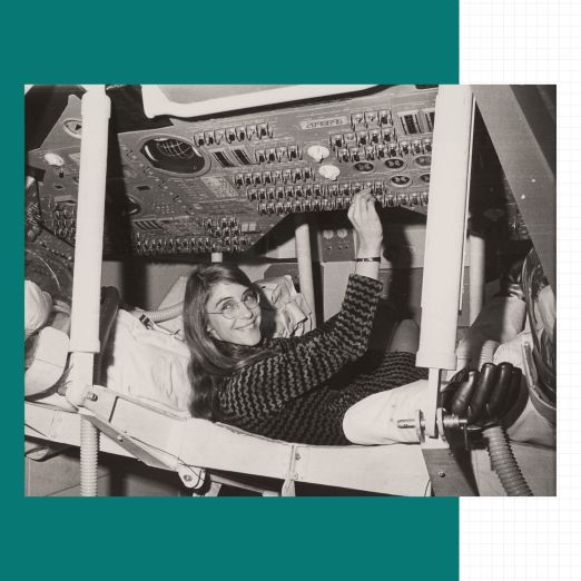 Margaret Hamilton liegt in einem Raumschiff und drückt an einer Schaltanlage einen von vielen verschiedenen Knöpfen.