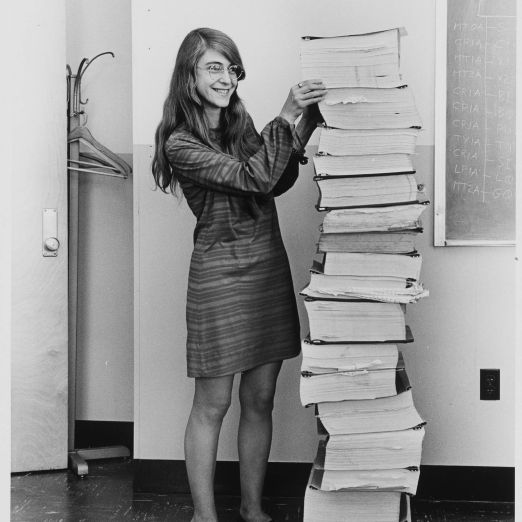 Margaret Hamilton steht neben dem ausgedruckten Code für die Apollo-Flugsoftware, ein Papierstapel der so groß wie sie selbst ist.