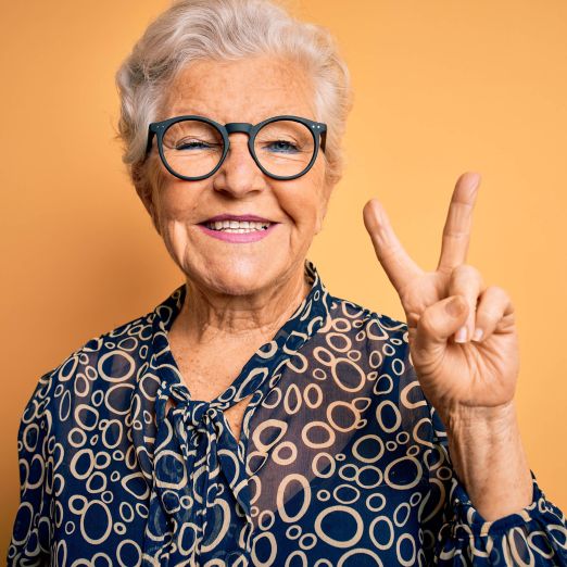 Eine lachende ältere Dame macht das Peace-Zeichen mit ihrer Hand.
