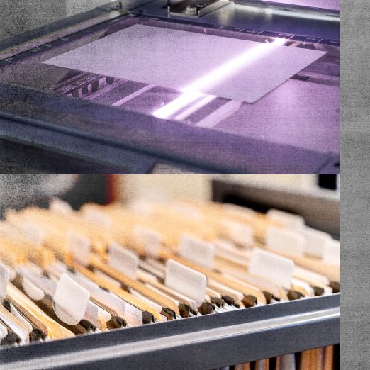 Ein geöffneter Scanner, auf dem ein Blatt Papier gerade gescannt wird und verschiedene sortierte Akten in einer Schublade.