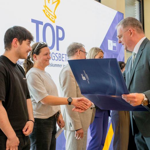Foto von Auszubildendem Elias Heuer und Ausbildungskoordinatorin Simone Bartels, wie sie die Urkunde zum Top Ausbildungsbetrieb 2026 von IHK-Präsident Matthias Belke überreicht bekommen
