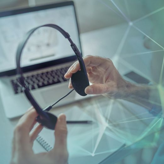 Büroangestellter hält Headset vorm Computer in Hand
