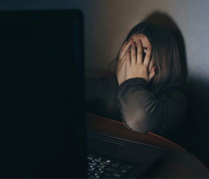 Bild: Ein Mädchen sitzt an einem Tisch vor einem Laptop und verbirgt ihr Gesicht in ihren Händen.