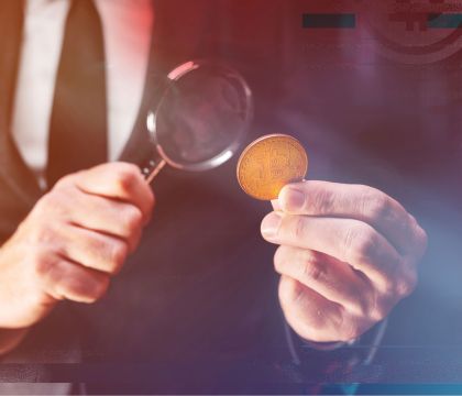 Mann, der mit einer Lupe eine Münze untersucht