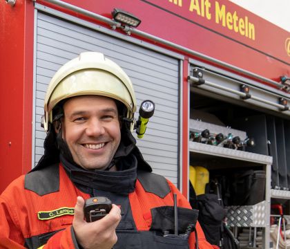 DVZ-Mitarbeiter Christian Lampe im Feuerwehranzug vor einem Feuerwehrauto stehend