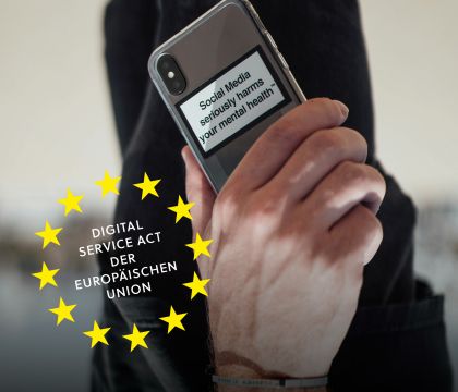 Eine Hand hält ein Smartphone, auf dem ein Warnhinweis zur Nutzung von sozialen Medien angebracht ist