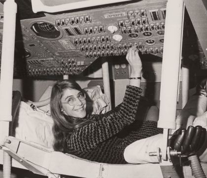 Margaret Hamilton liegt in einem Raumschiff und drückt an einer Schaltanlage einen von vielen verschiedenen Knöpfen.