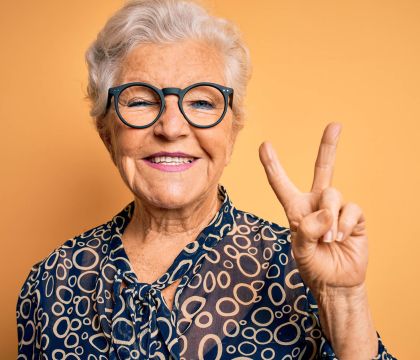 Eine lachende ältere Dame macht das Peace-Zeichen mit ihrer Hand.